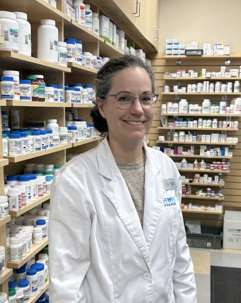 Pharmacist standing by shelves with medicine bottles.