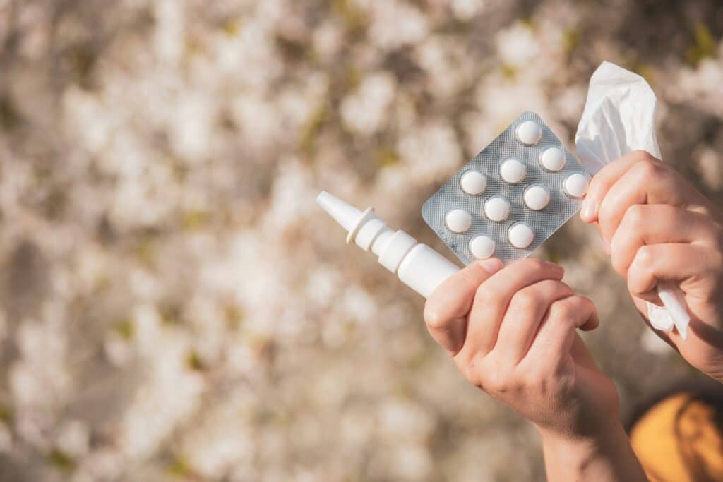Hands holding allergy medicine and tissue.